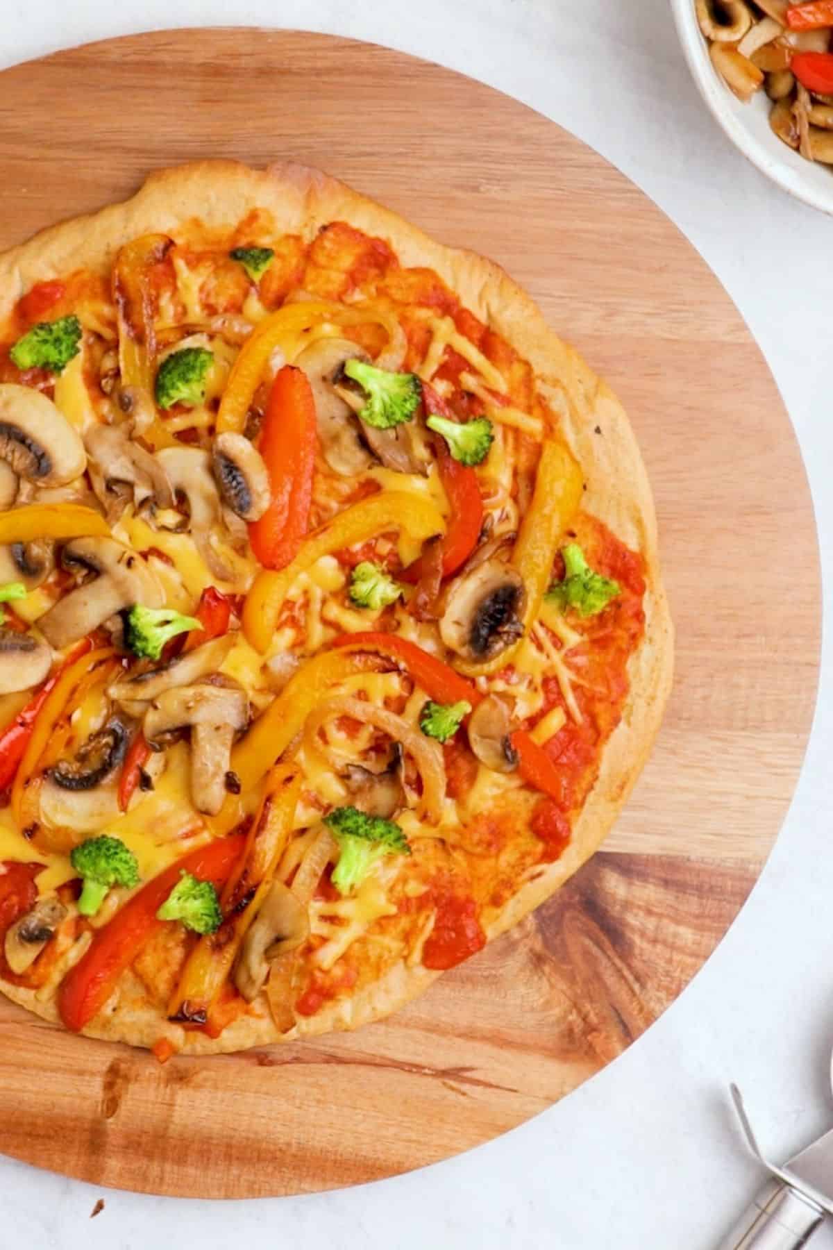 Round pizza on cutting board with sauce, cheese and grilled veggies on top.