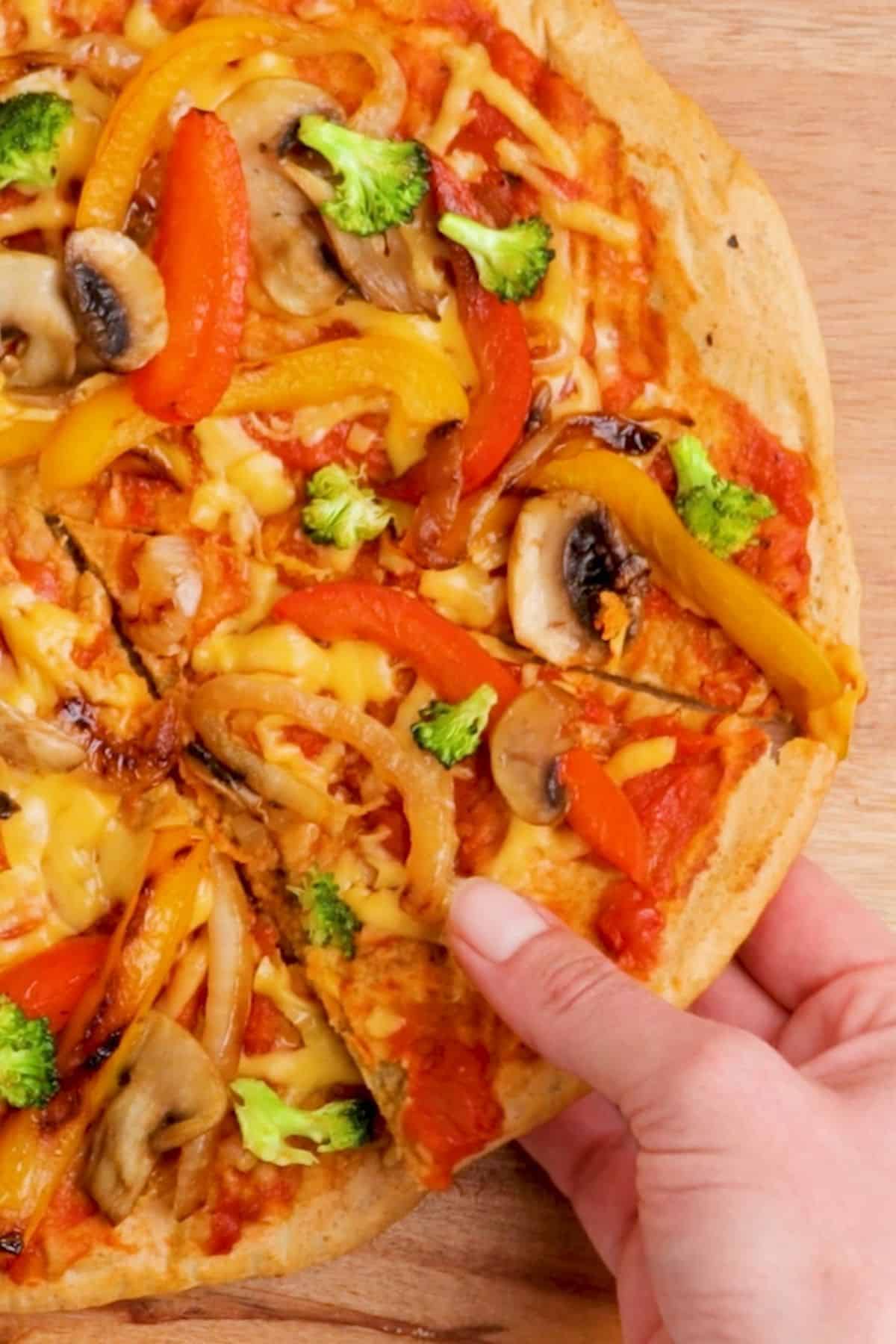 hand lifting slice of pizza from cutting board.