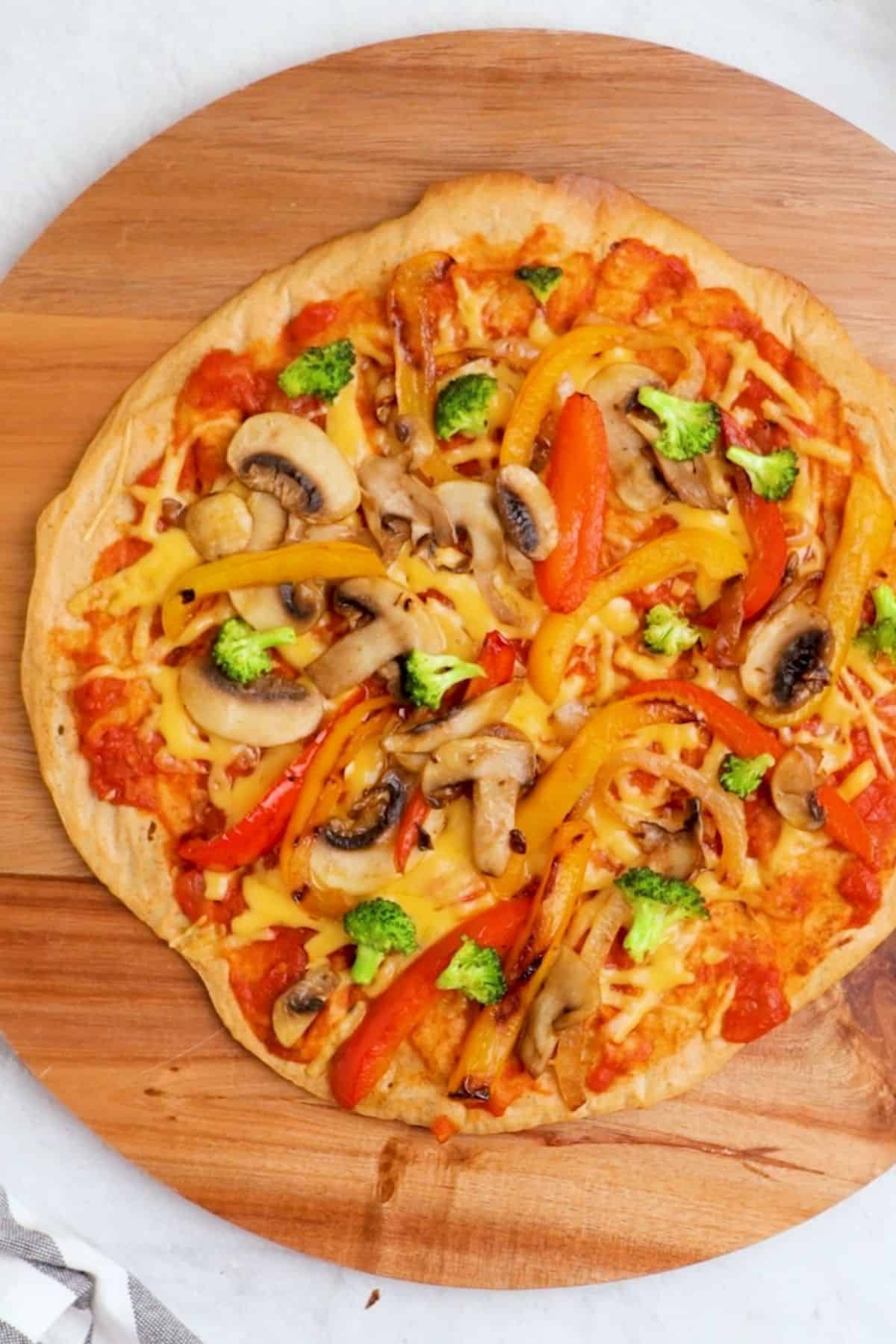 Lentil pizza crust on cutting board with sauce, cheese and grilled veggies on top.