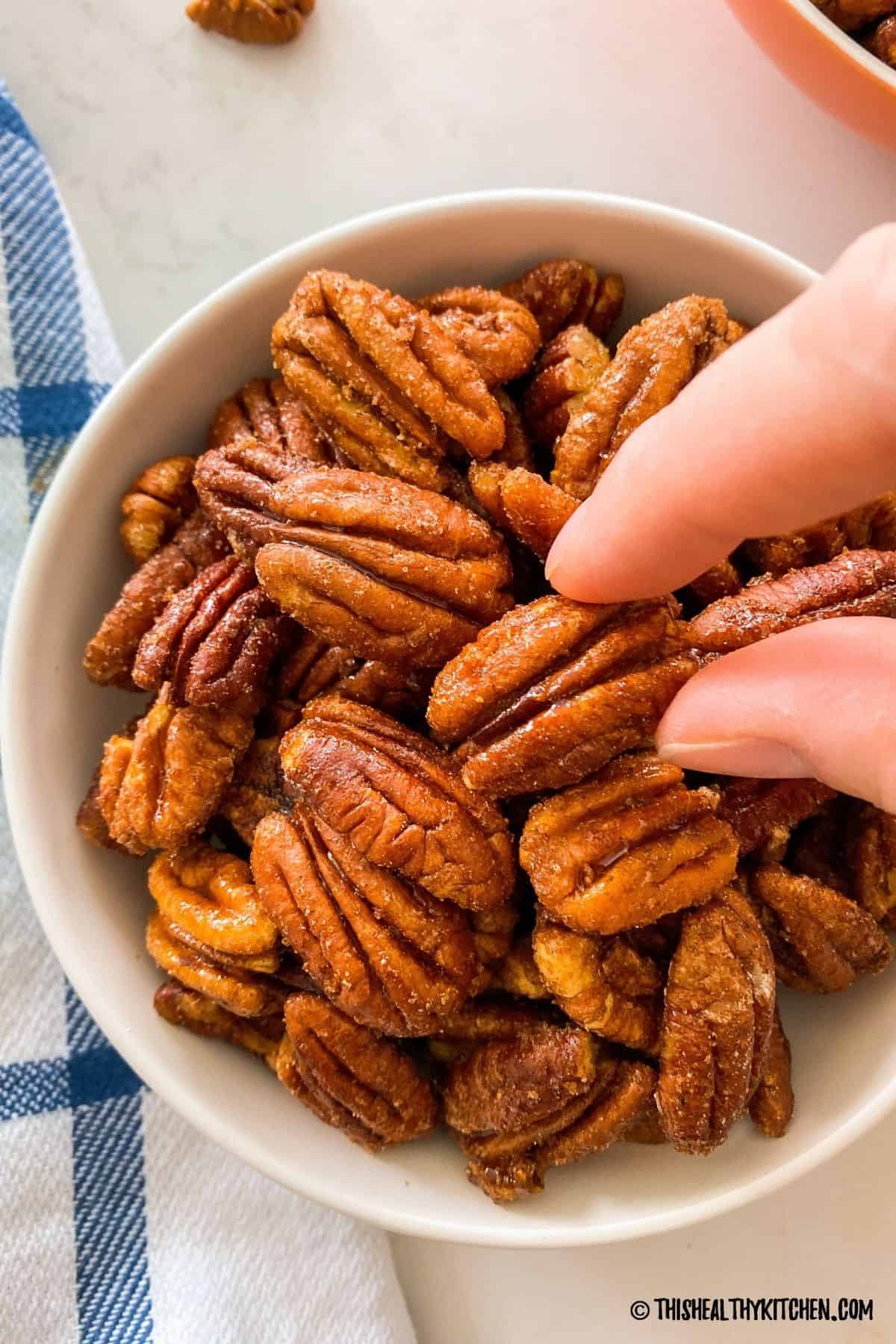 Bowl of candied pecans with hand grabbing one.