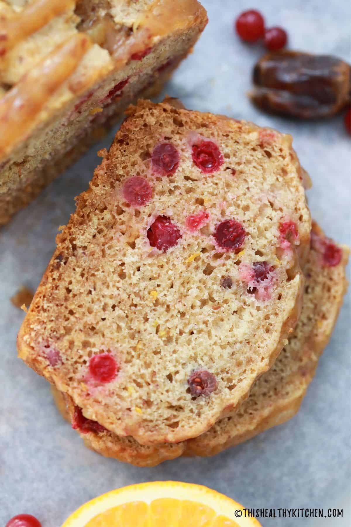 Two slices of stacked sweet bread with cranberries and loaf beside it.