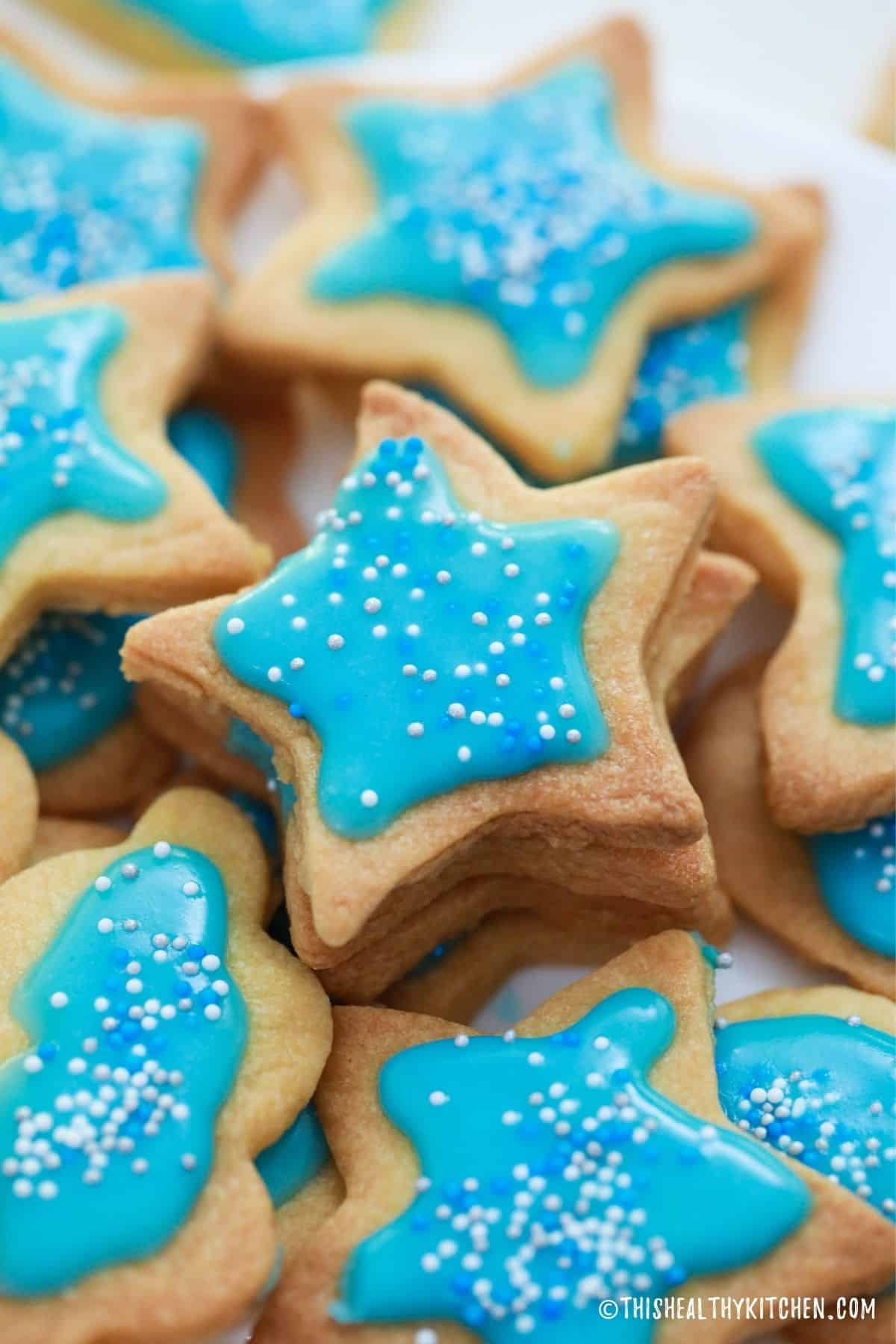 Stacks of star shaped shortbread cookies with blue icing and sprinkles on top.