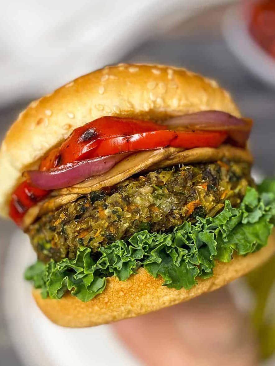 hand holding up veggie burger with lettuce, onion, and peppers inside
