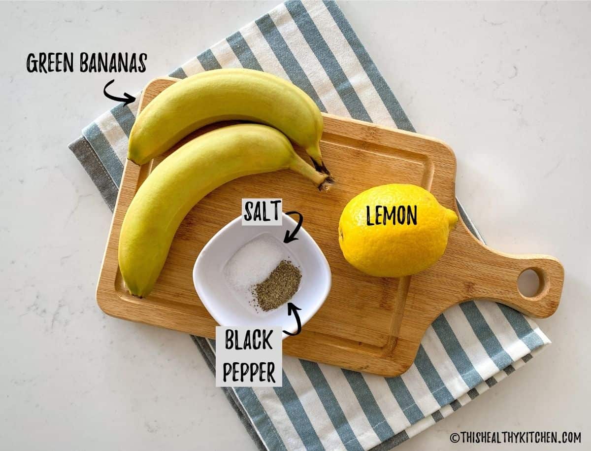 Green bananas, lemon, salt and pepper on cutting board.