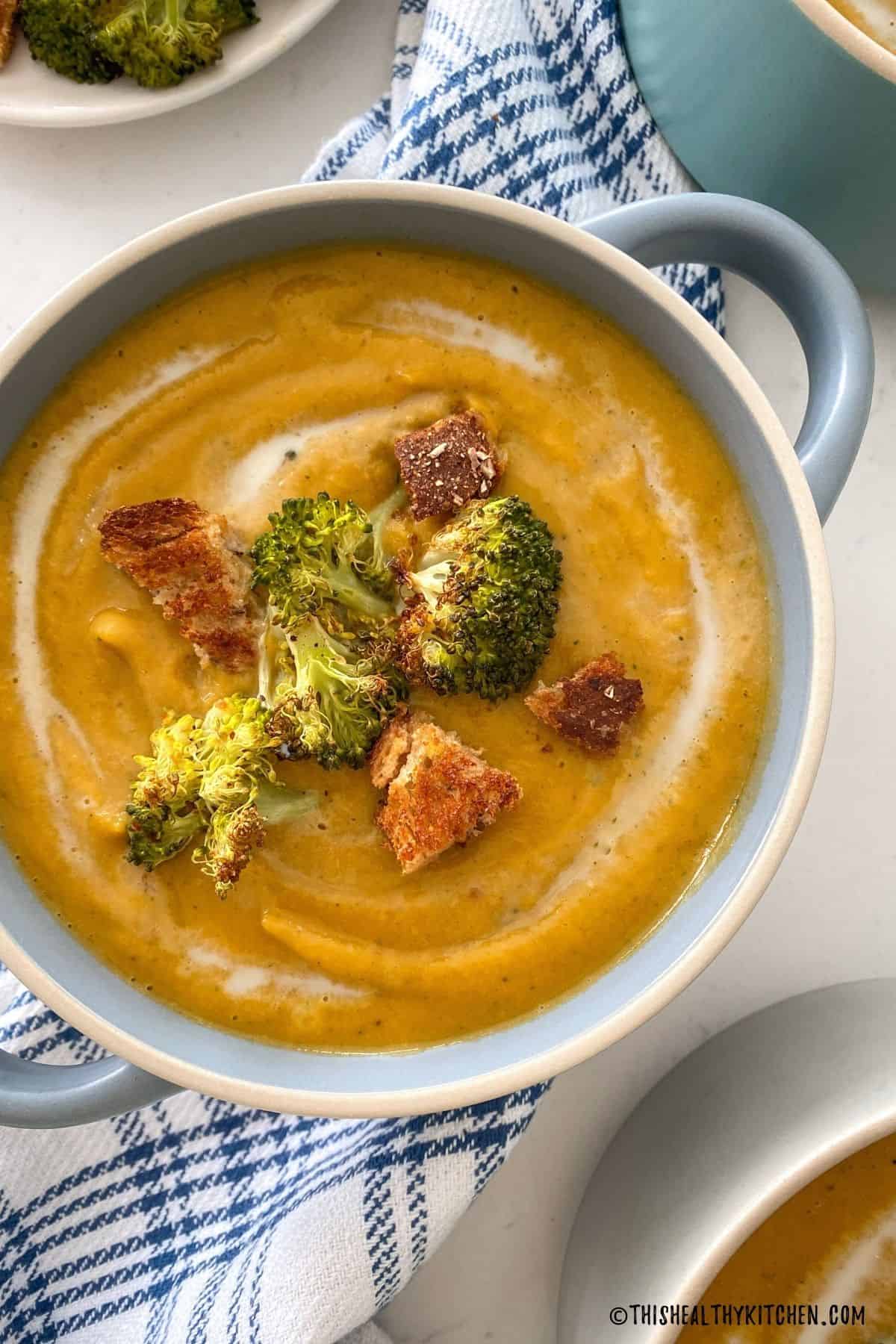 Blue bowl filled with broccoli and sweet potato soup with broccoli florets and croutons on top.