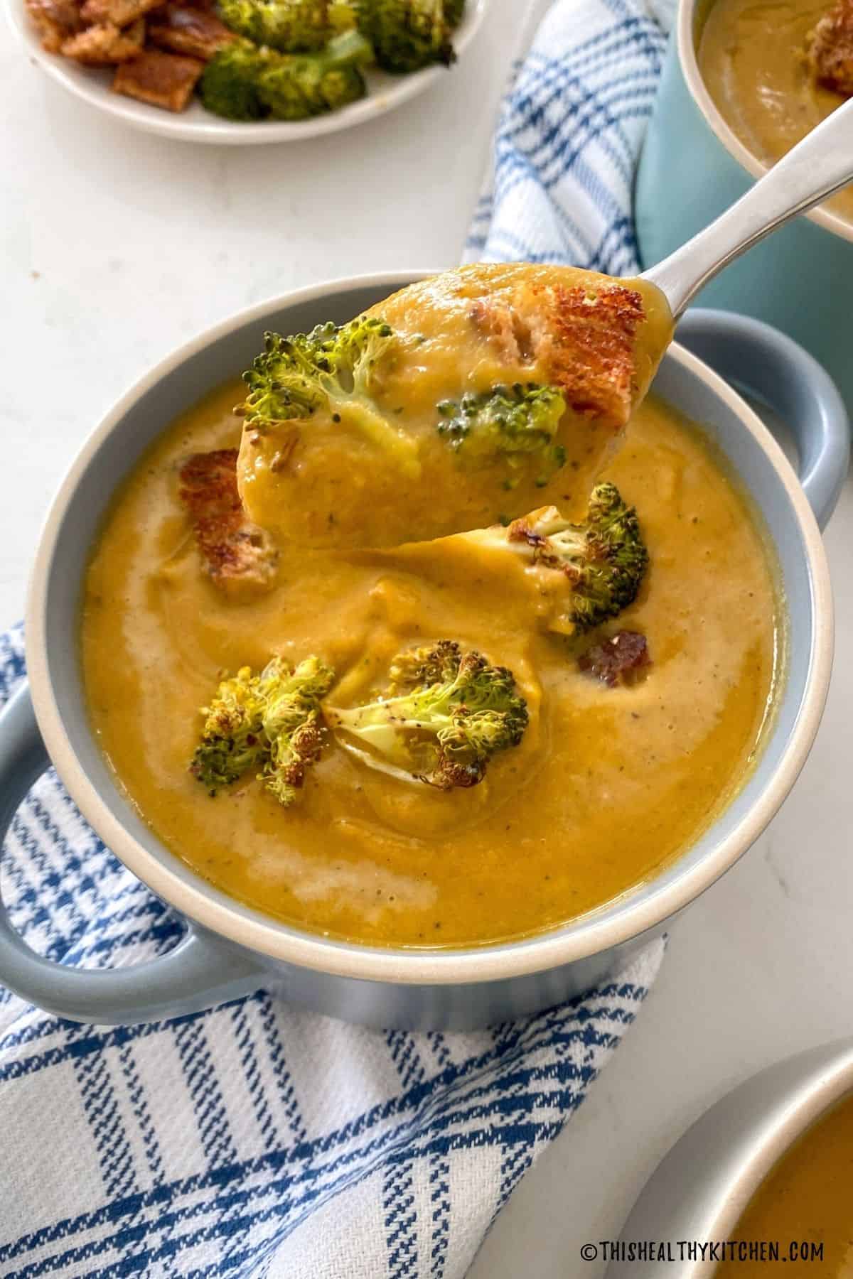 Spoon of broccoli sweet potato soup being lifted over bowl of soup.