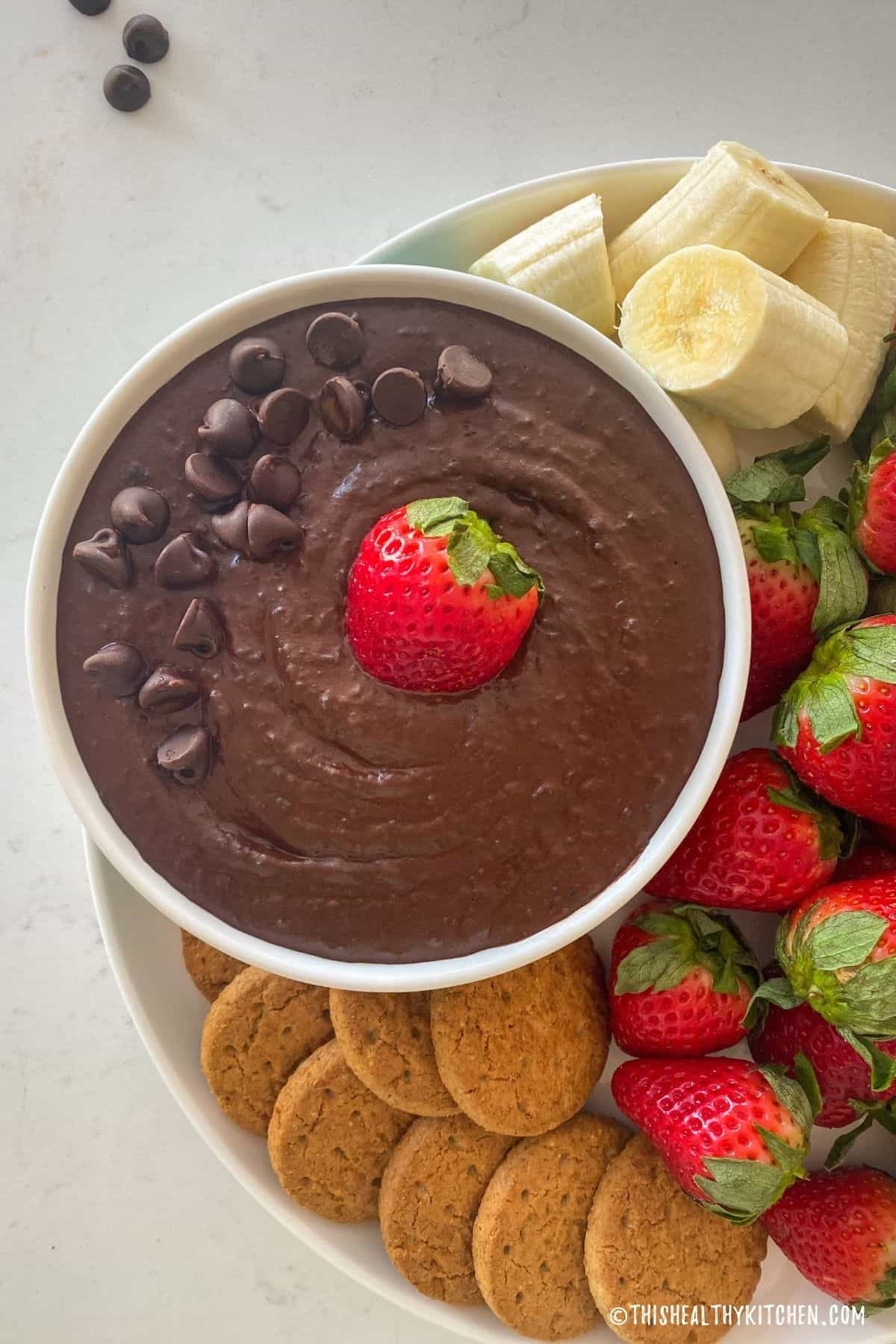 Bowl of chocolate hummus with a strawberry in the center and cookies and banana slices around it.