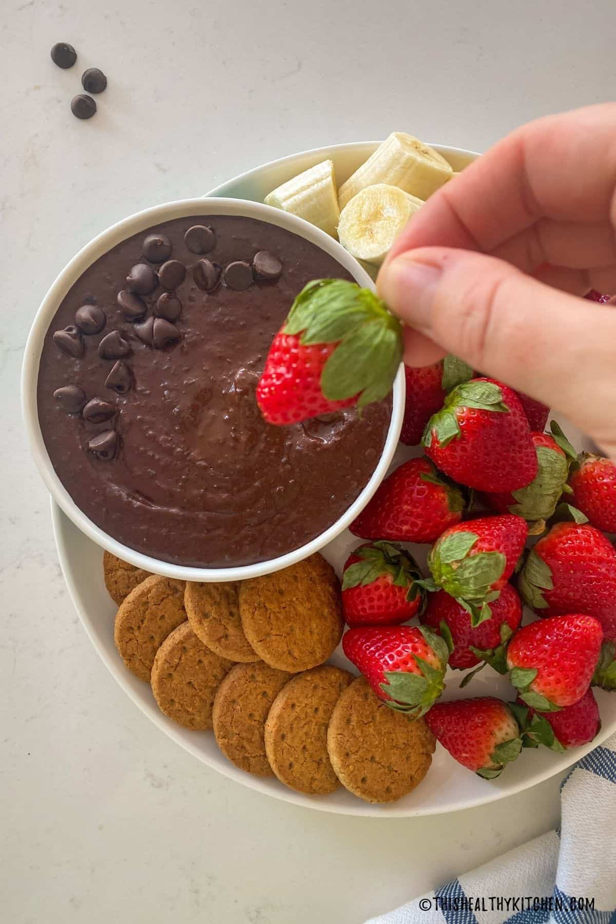 Hand holding strawberry above bowl of chocolate dip.