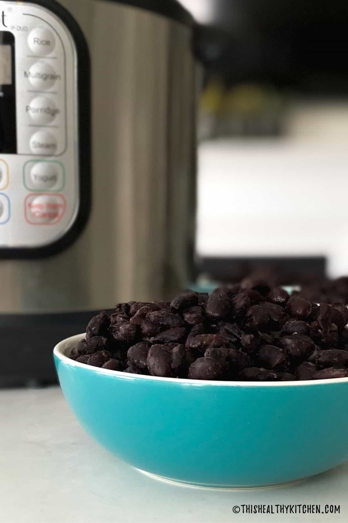 Blue bowl filled with cooked black beans and Instant Pot in the background.