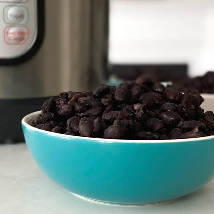 Blue bowl filled with cooked black beans and Instant Pot in the background.