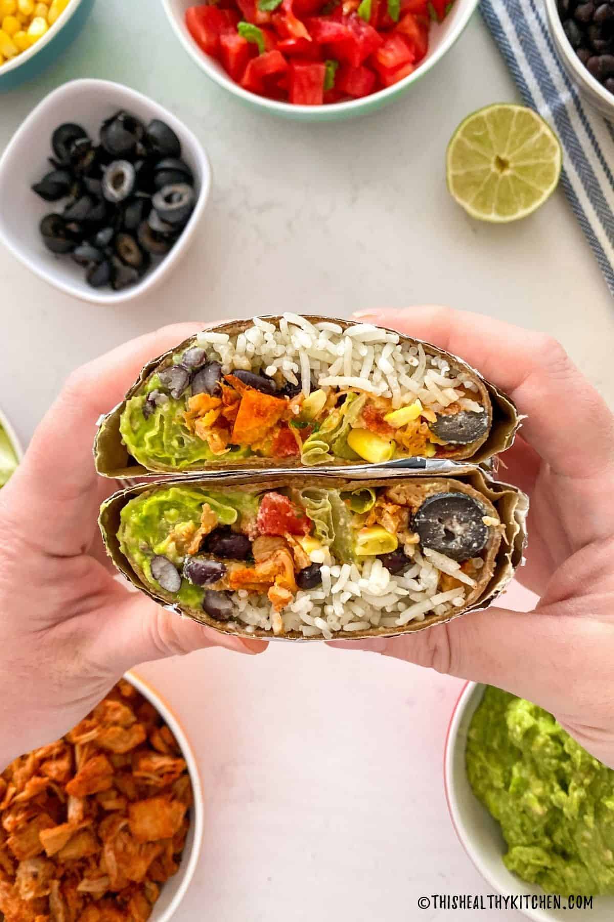 Hands holding up jackfruit burrito that is cut in half.