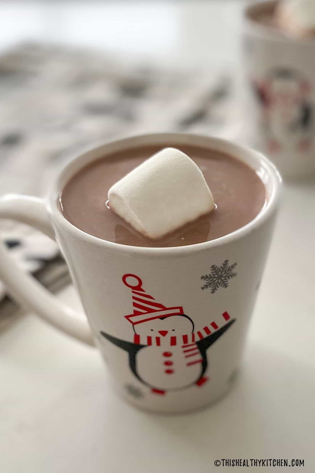 Mug with penguin on it, filled with hot chocolate and 1 big marshmallow on top.