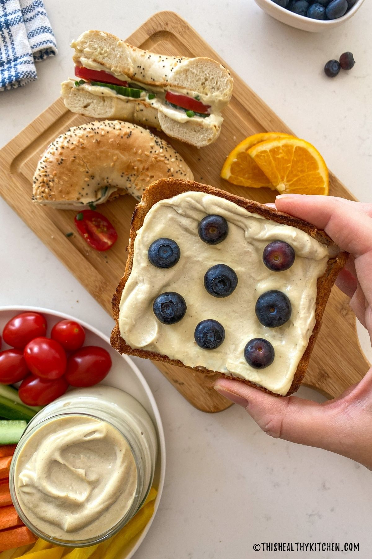 Hand holding slice of toast with cream cheese and blueberries on top.