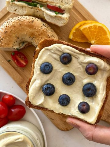 Hand holding slice of toast with cream cheese and blueberries on top.