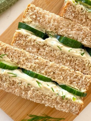 Cucumber and cream cheese sandwiches cut side up and sitting on cutting board.