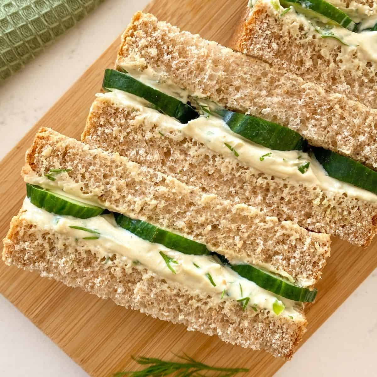 Cucumber and cream cheese sandwiches cut side up and sitting on cutting board.