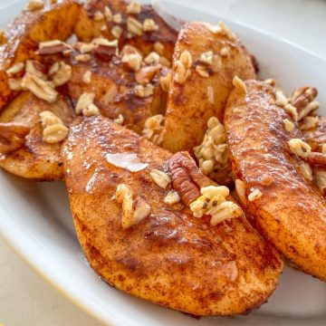 Air fried pears in white dish with granola and chopped nuts on top.