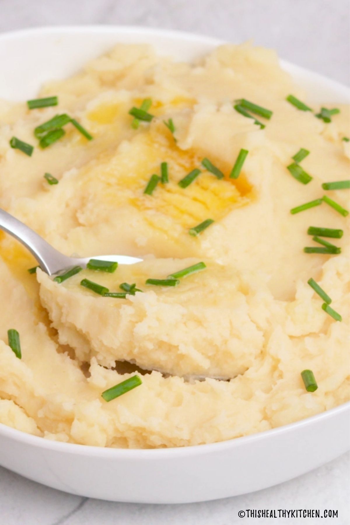 Spoon scooping up mashed potatoes from bowl.