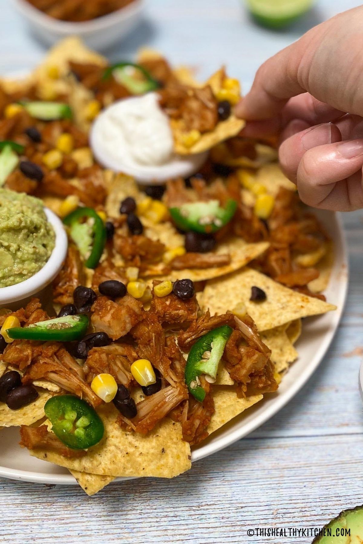 Chip being dunked into bowl of sour cream in the center of a platter of nachos.