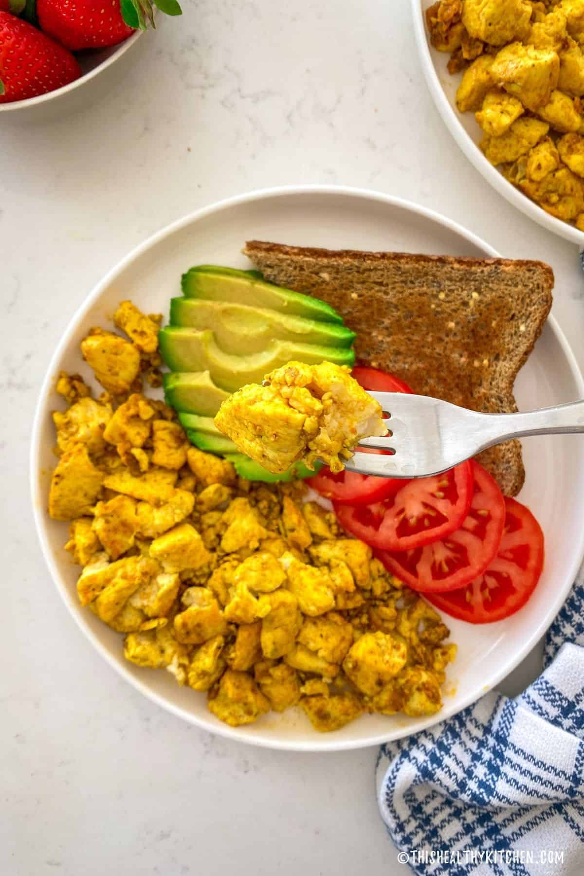 Fork full of vegan scrambled eggs being held over plate below.