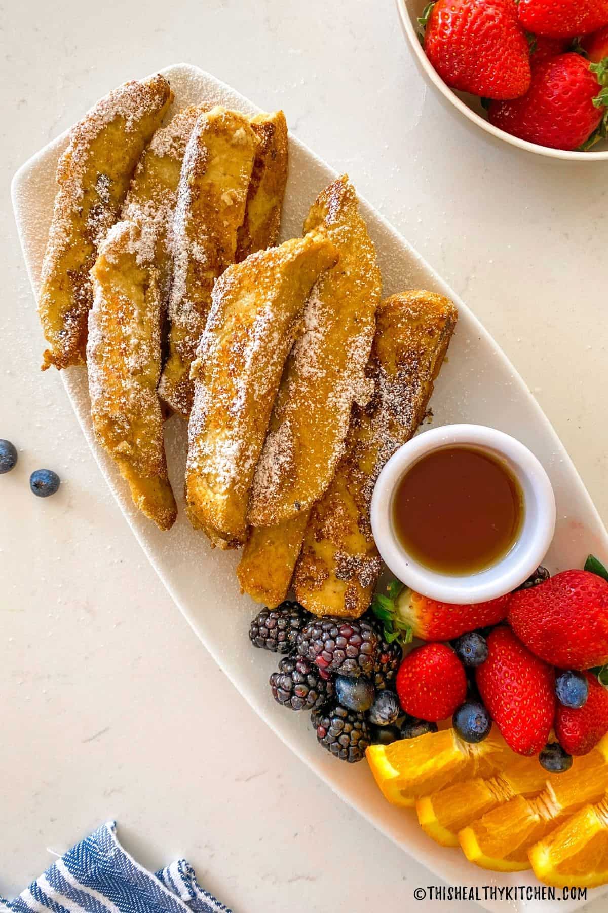 French toast sticks with powdered sugar sprinkled on top and maple syrup for dipping.