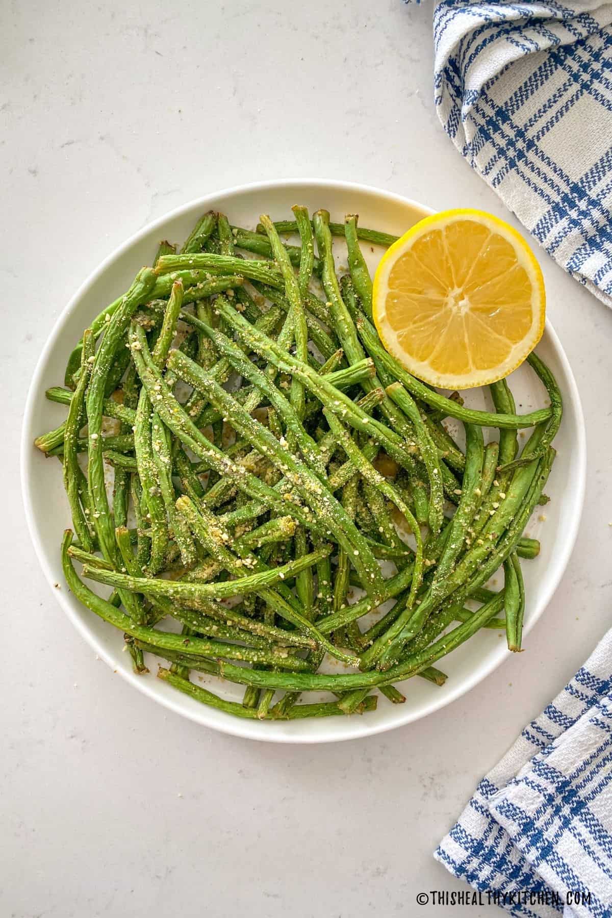 Cooked green beans in white plate with lemon on the side.