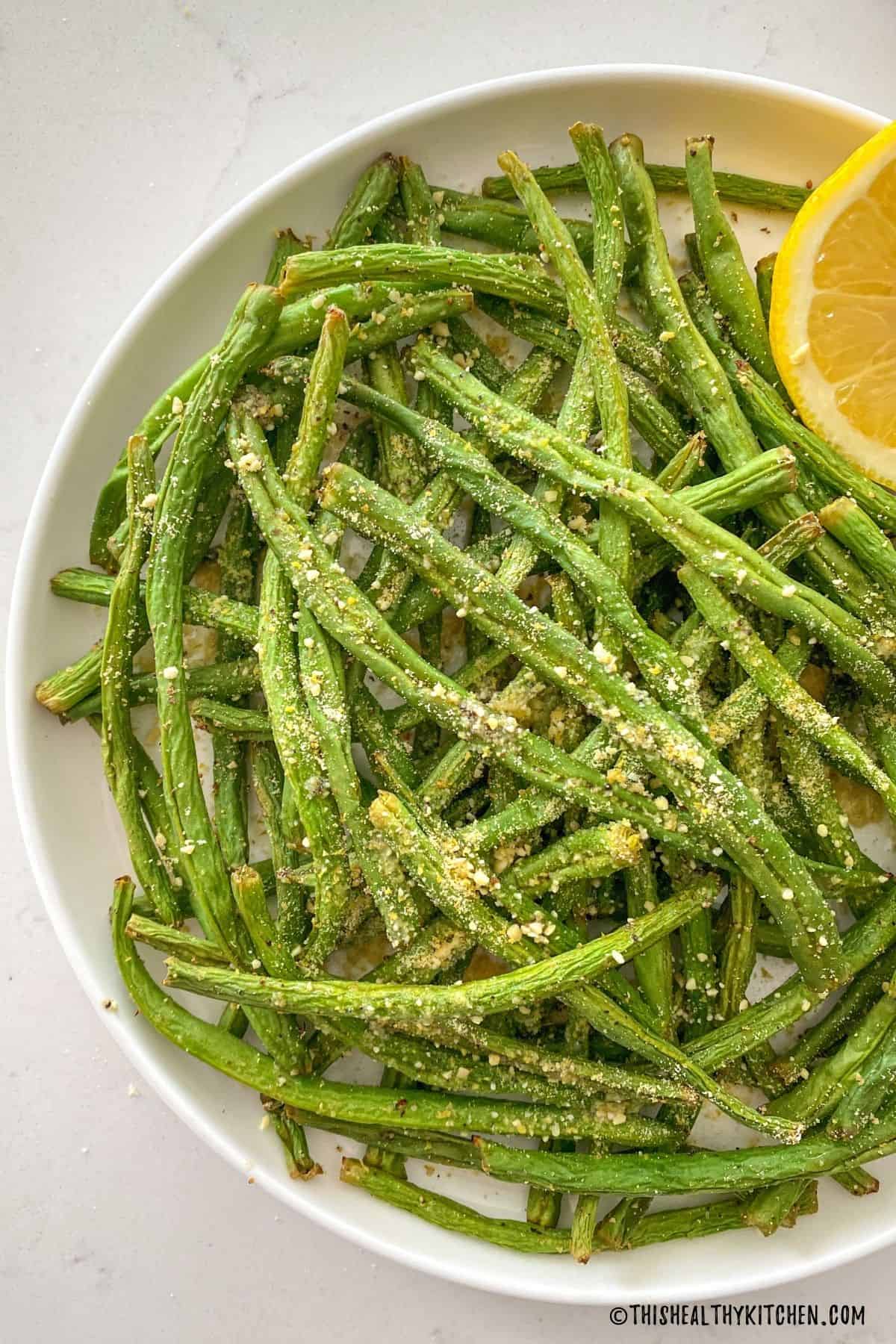 Plate of green beans with vegan parmesan cheese sprinkled on top.