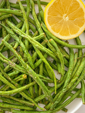 Green beans in white plate with halved lemon on the side.