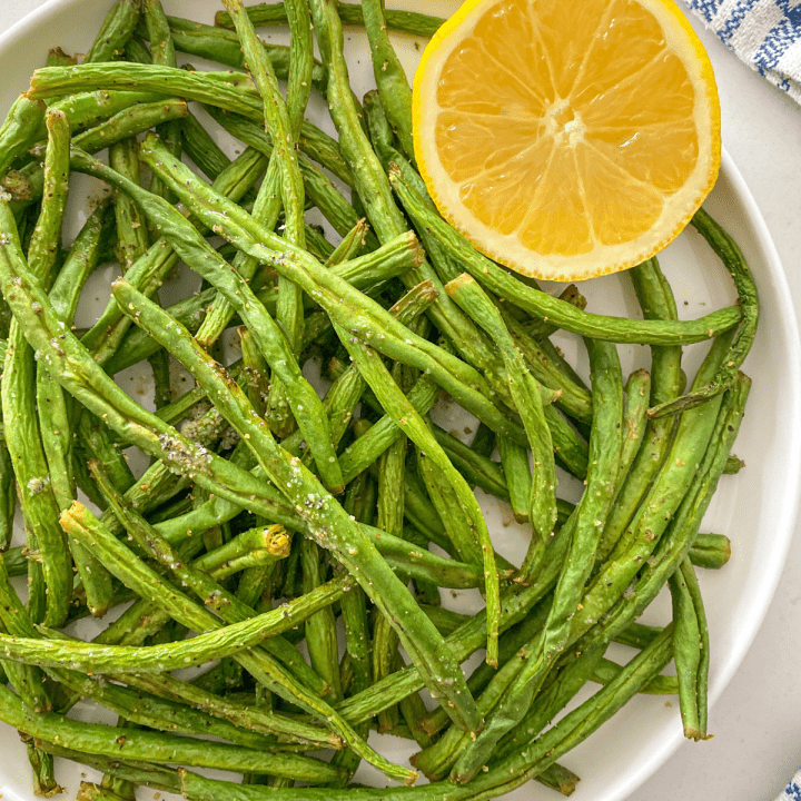 Green beans in white plate with halved lemon on the side.
