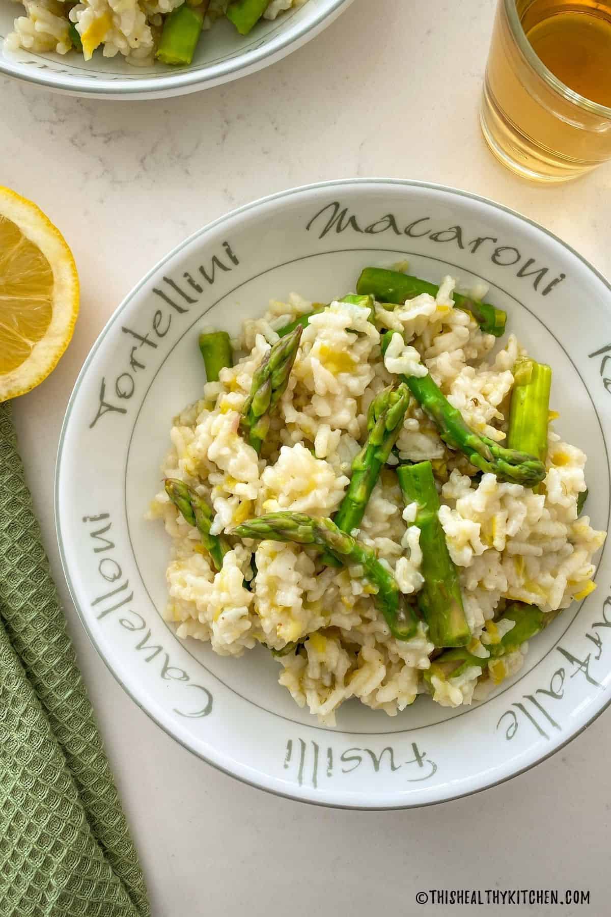 Risotto with asparagus in round bowl with lemon on the side.