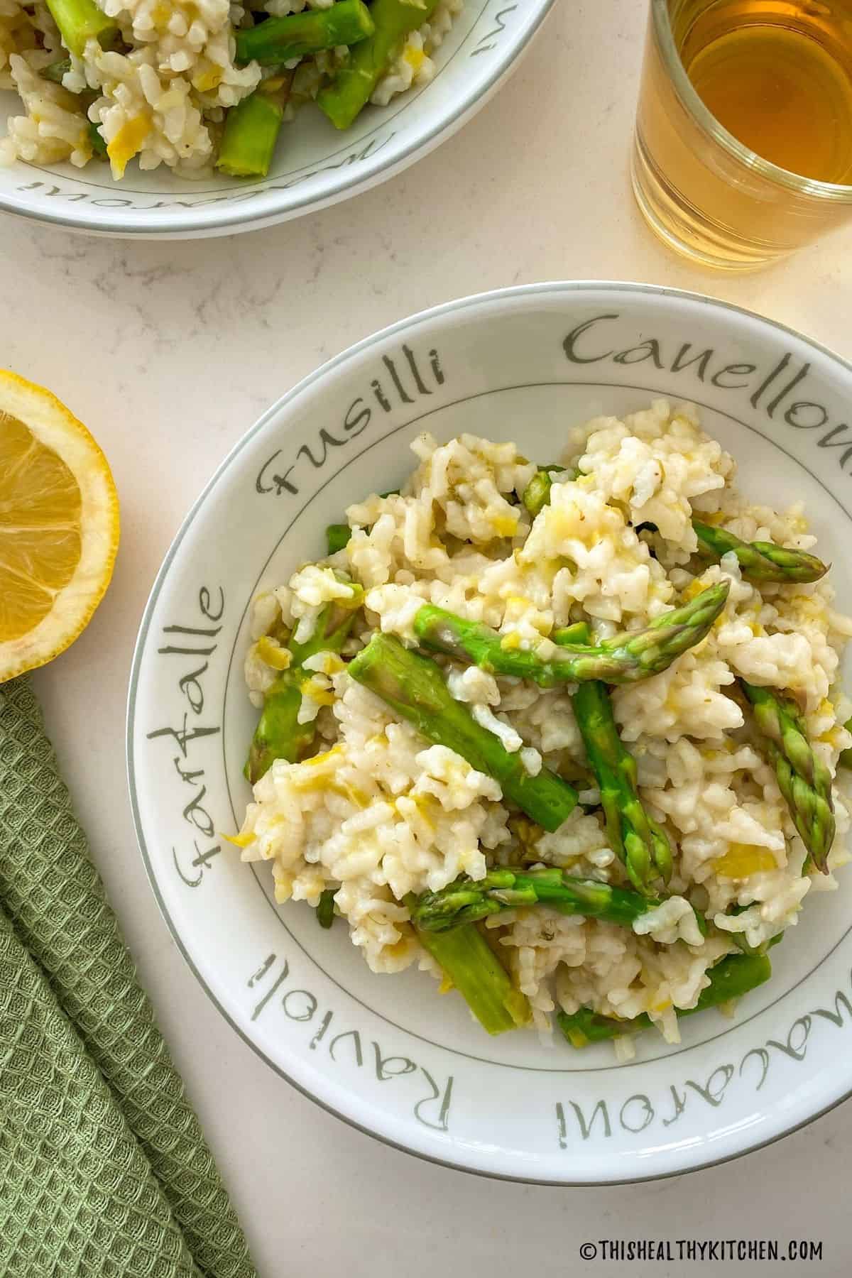 Two plates of asparagus risotto with glass of white wine above.