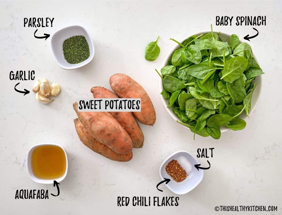 Sweet potatoes, bowl of spinach, garlic and bowls of seasoning on kitchen counter top.