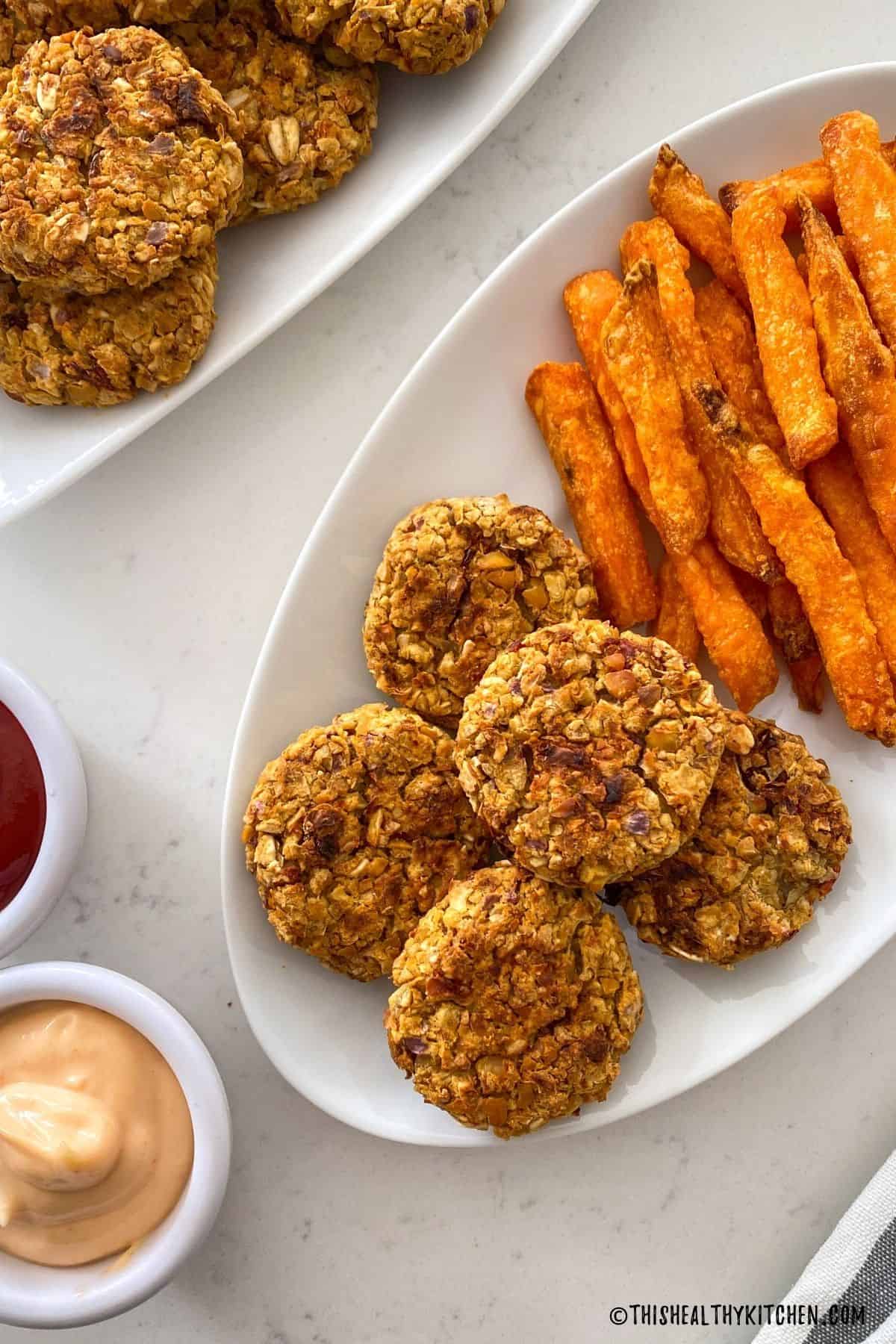 Chickpea nuggets in white dish with sweet potato fries beside it and dipping sauce on the side.