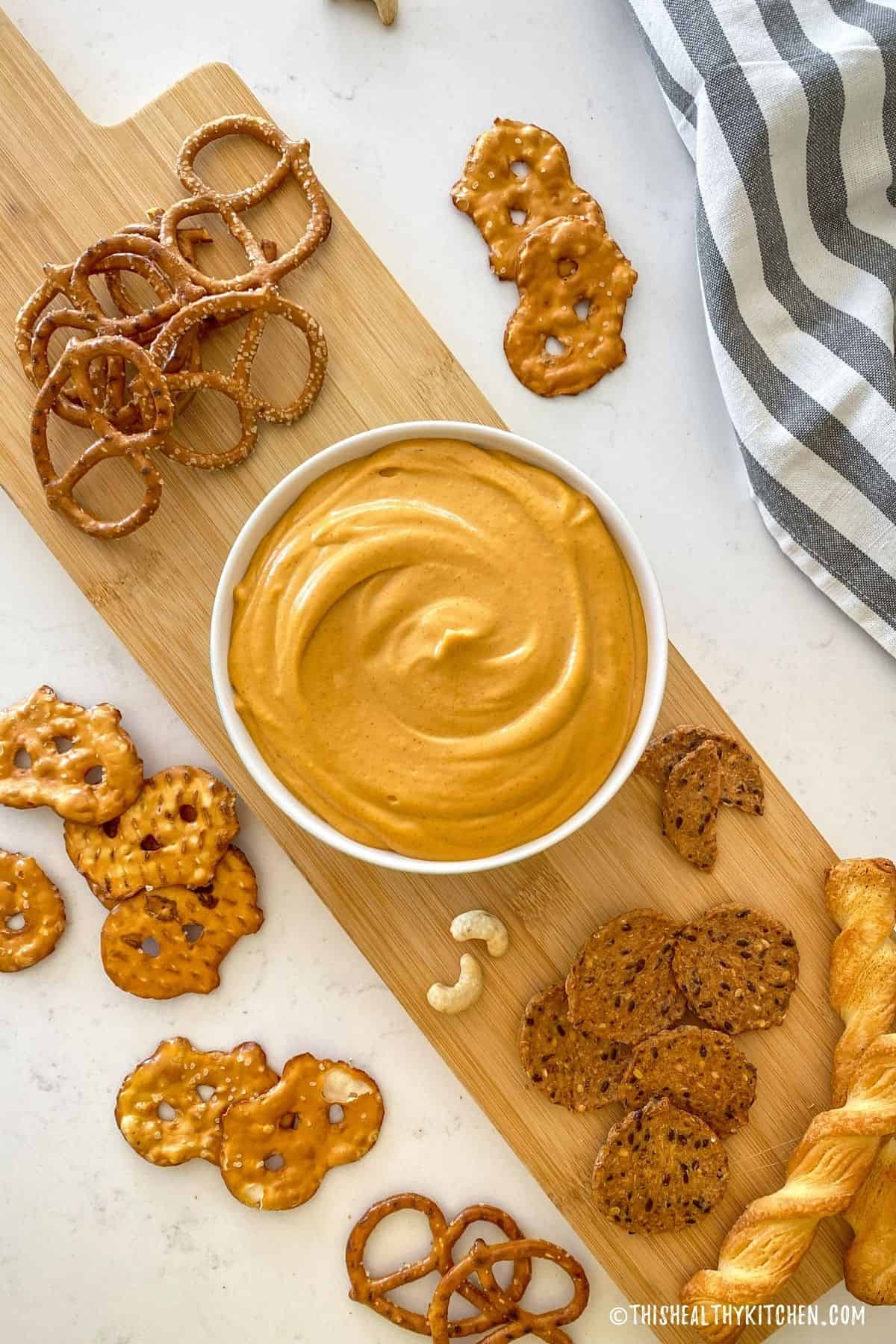 Beer cheese dip in bowl with crackers and pretzels around it.