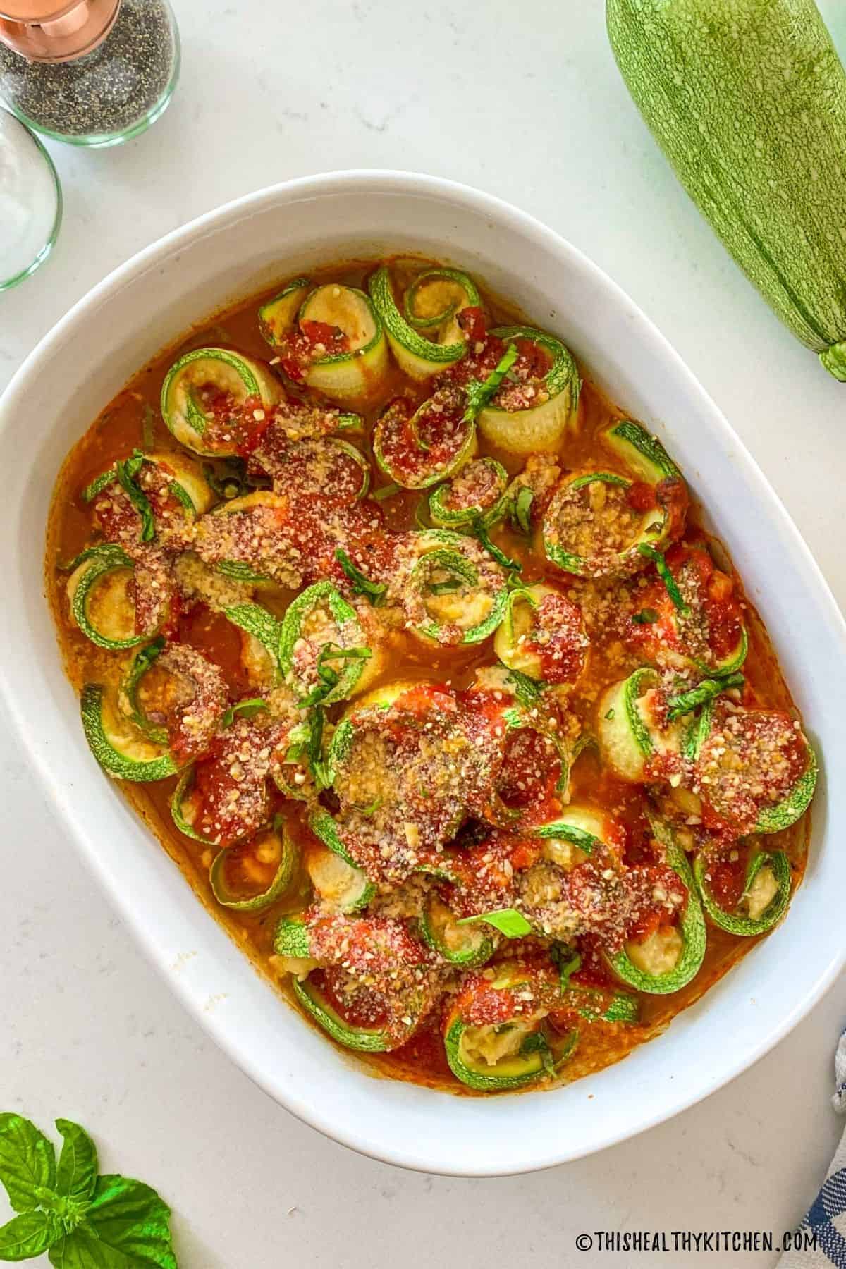 Large baking dish filled with cooked zucchini rolled up with ricotta cheese inside.