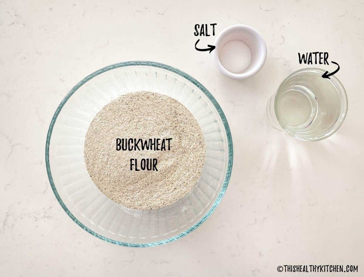 Bowl of buckwheat flour, cup of water and small bowl of salt on kitchen counter top.