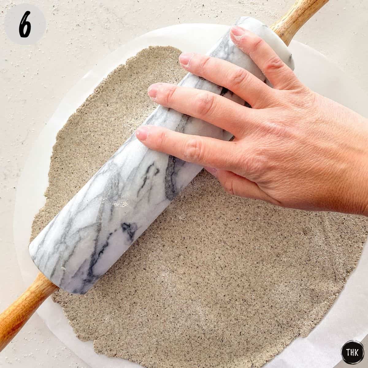 Hand using rolling pin to stretch pizza dough.