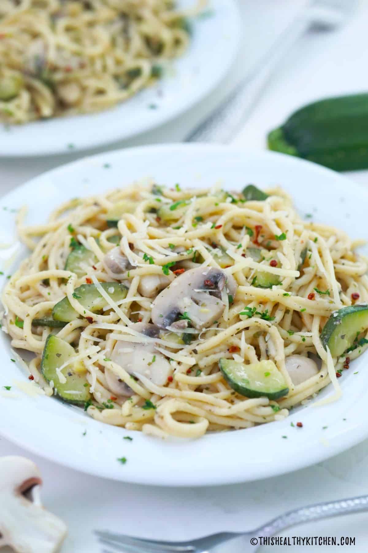 Side view of plate of spaghetti with mushrooms and zucchini on top.