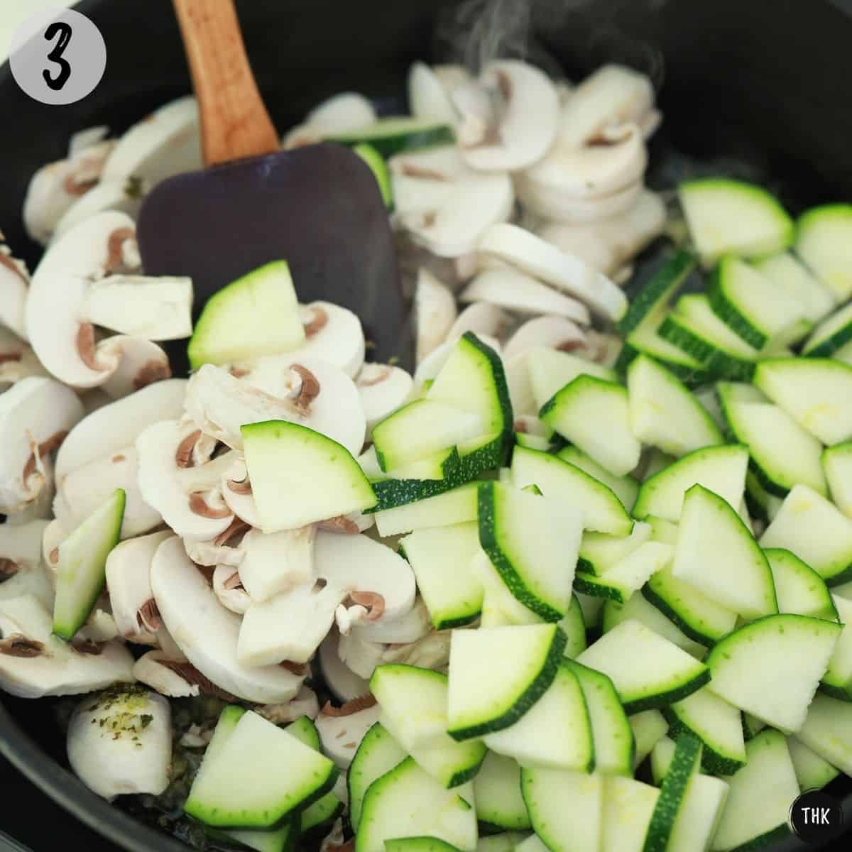 Mushrooms and zucchini slices being stirred in large pan.