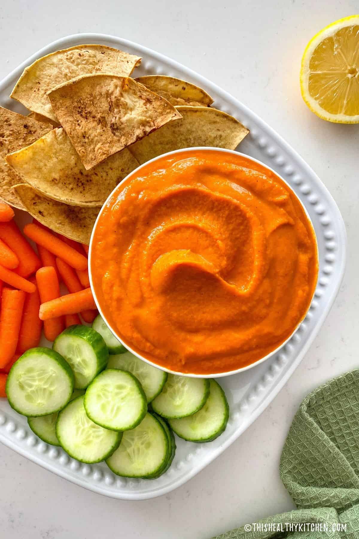 Orange dip in bowl with raw veggies and chips around it.