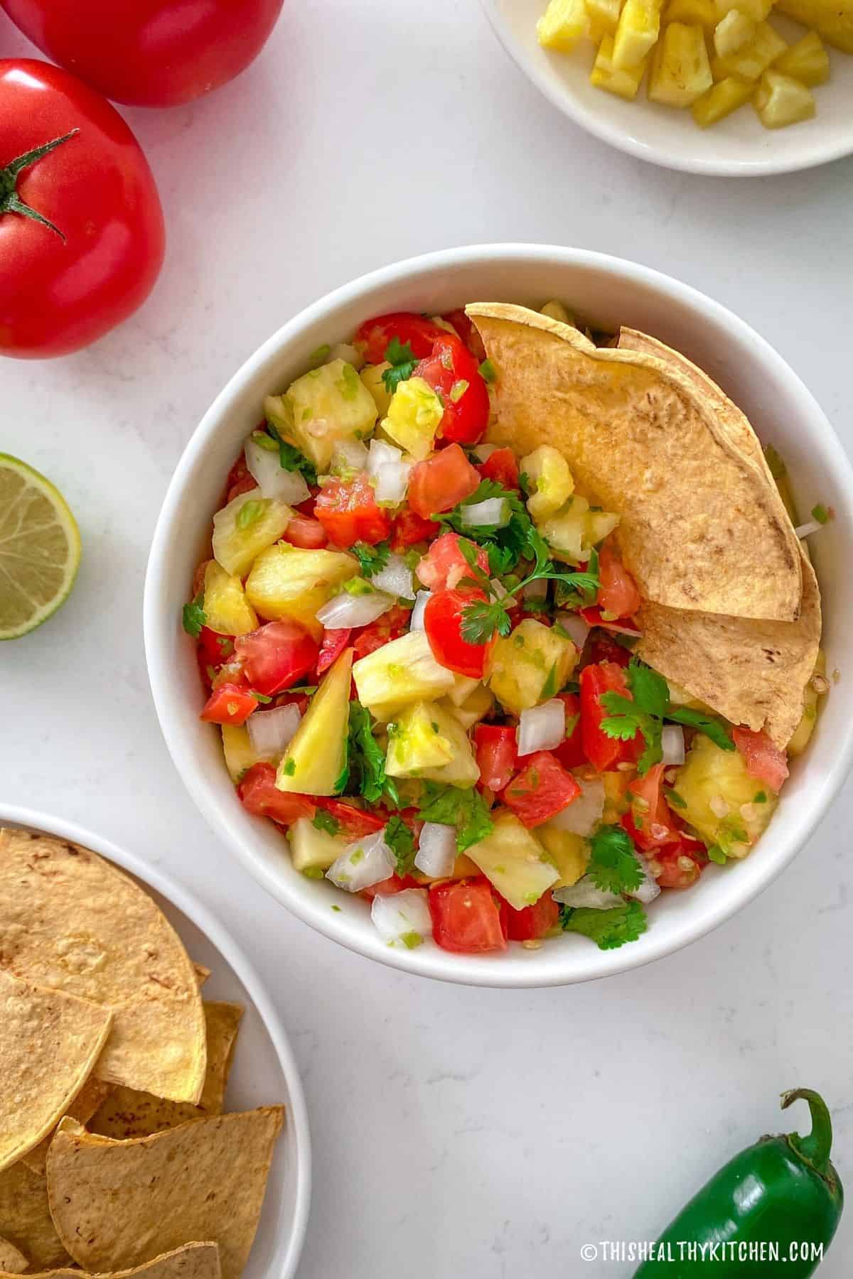 White bowl of pineapple pico de gallo with two chips standing up inside it.