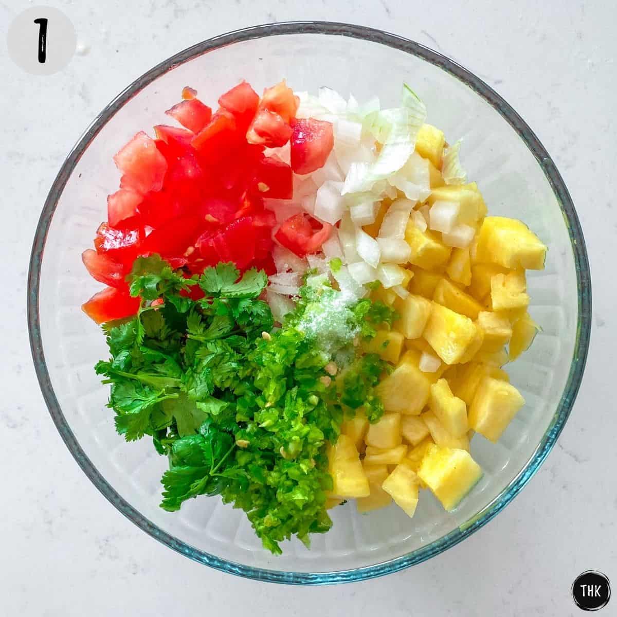 Large glass bowl with diced tomato, onion, pineapple and cilantro inside.
