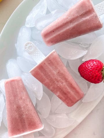 Three pink popsicles on tray filled with ice cubes.