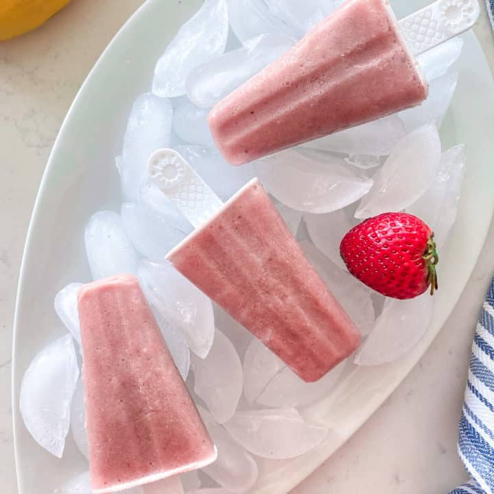 Three pink popsicles on tray filled with ice cubes.