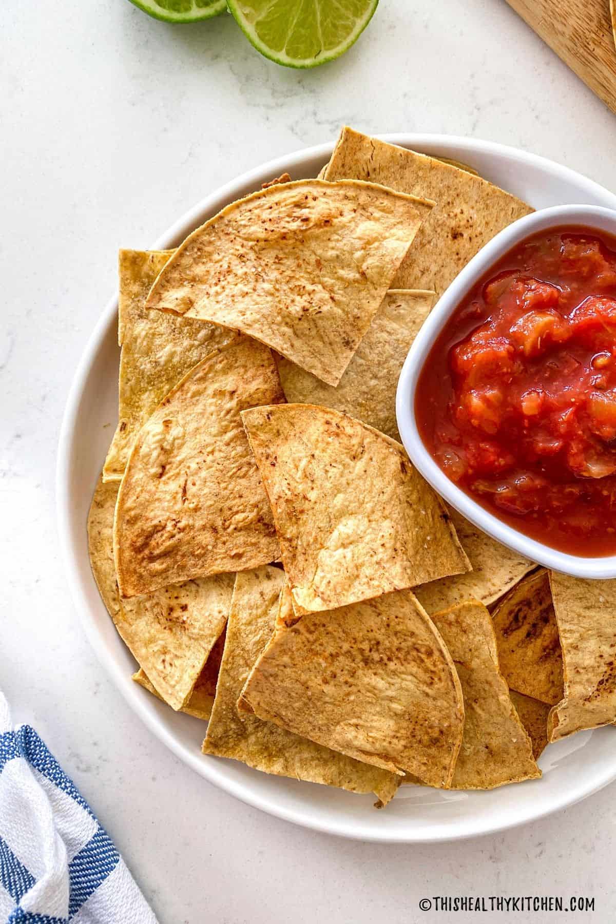 Homemade tortilla chips with bowl of red salsa beside them.