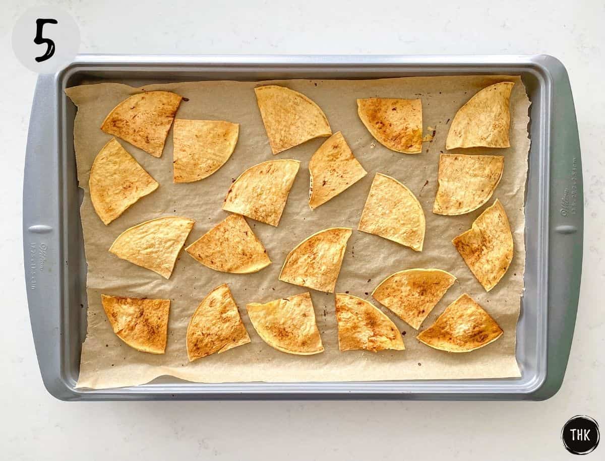Baked tortilla chips on baking tray lined with parchment paper.