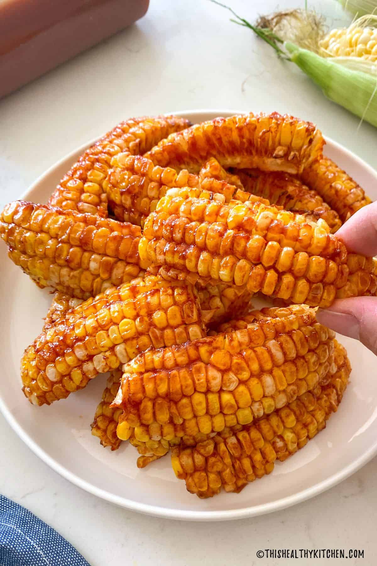 Hand picking up corn that's covered in bbq sauce.