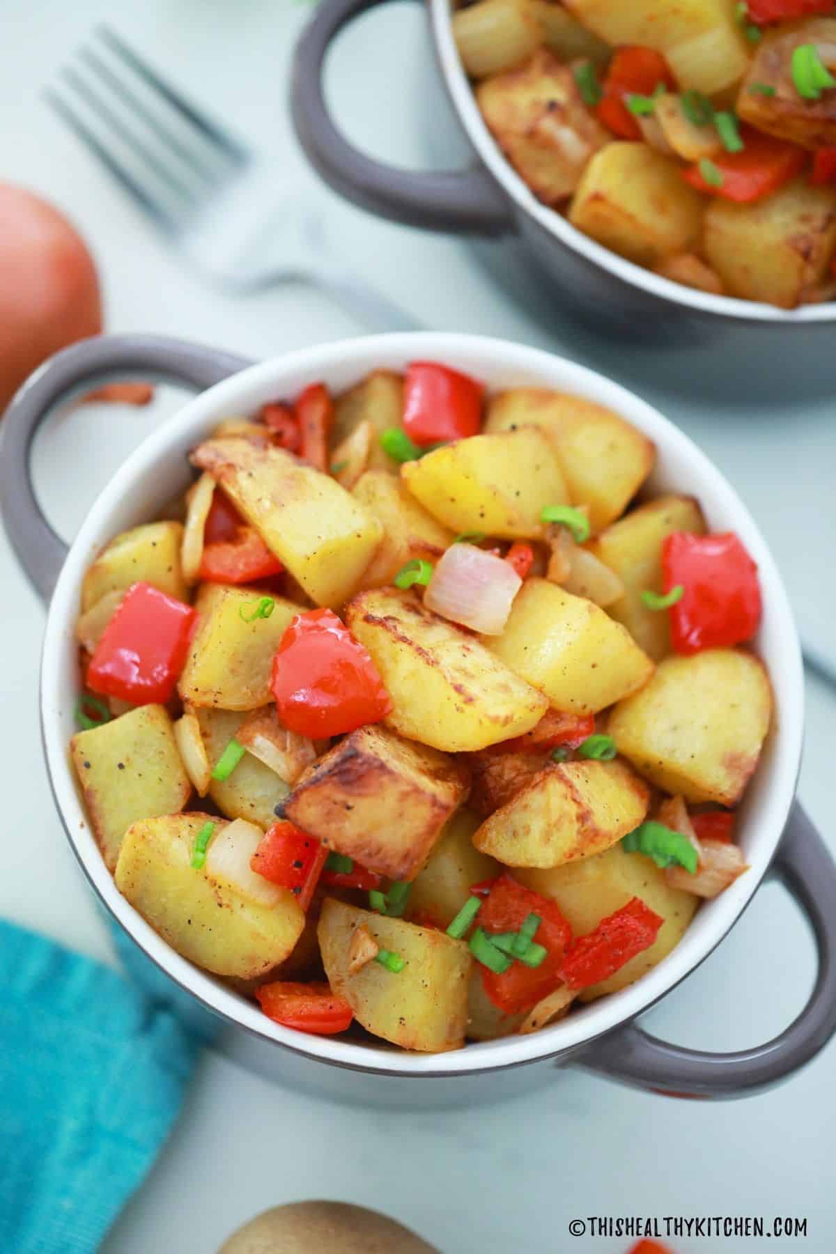 Bowl of breakfast potatoes with red pepper and onion on top.