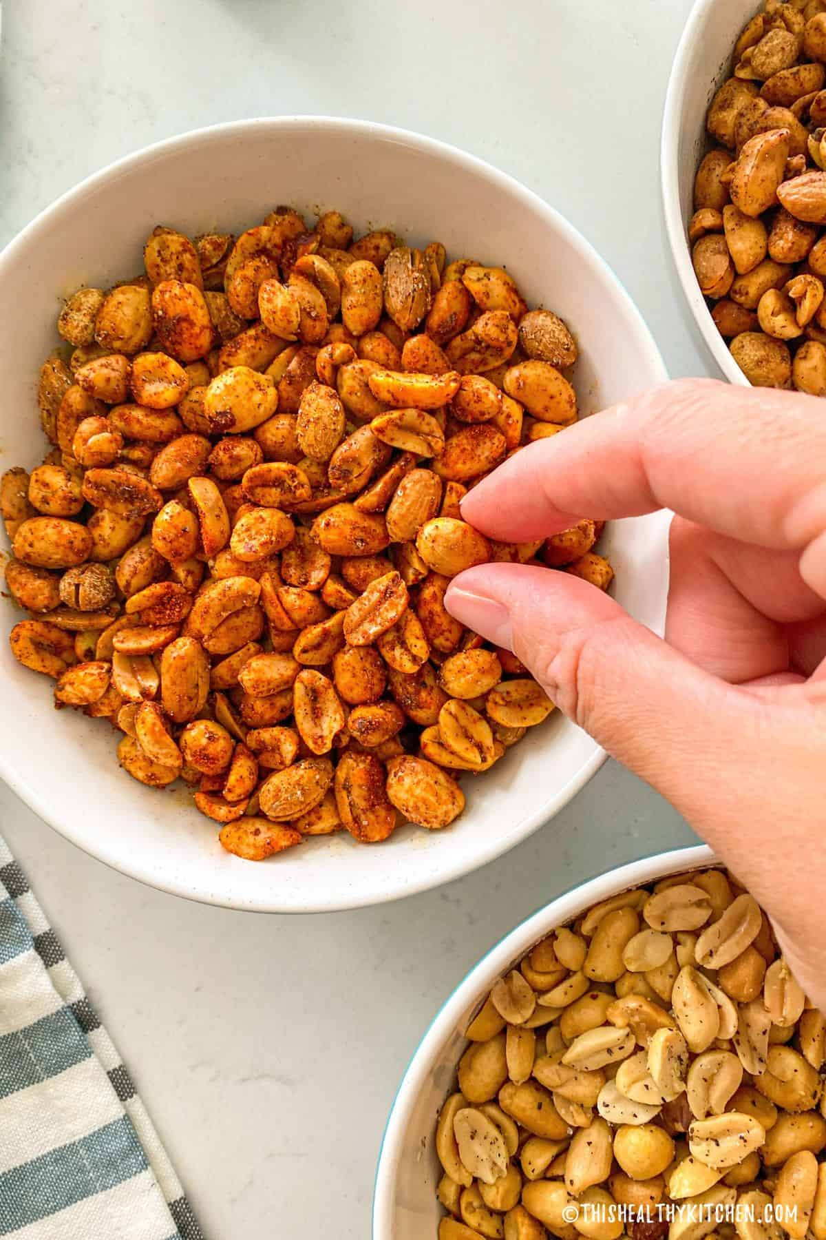 Hand reaching for roasted peanut in bowl of peanuts.