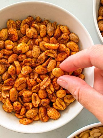 Bowl of air fried peanuts with hand grabbing one.